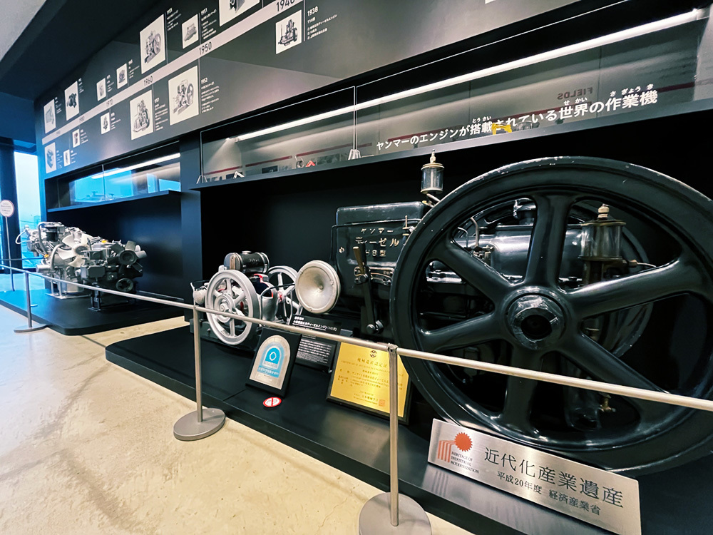 「ヤンマー 横形 水冷ディーゼルエンジンHB形」 (写真手前)。一般社団法人日本機械学会により「機械遺産」に、また、経済産業省より「近代化産業遺産」に認定されているほか、国立科学博物館の未来技術遺産 に登録された。(写真提供:ヤンマーミュージアム)