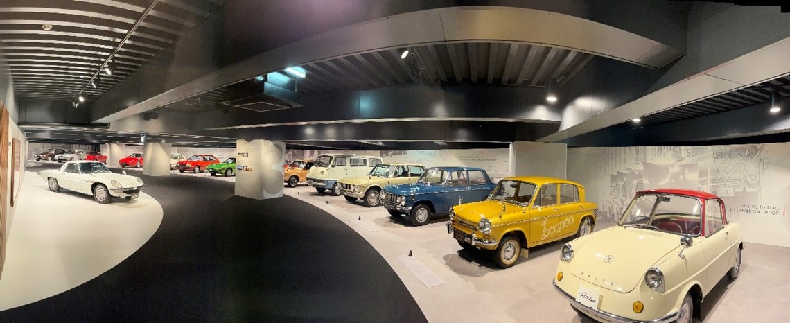 ZONE 1「ものづくり精神の原点」から続く「過去」を展示するZONE 2〜6。クルマたちが、世相を表す写真や社員の姿・言葉をバックに展示されている(筆者撮影)