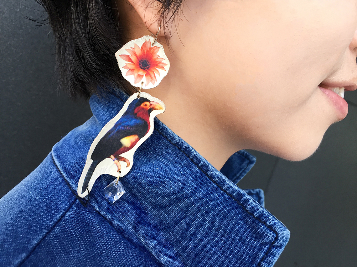 カラフルな鳥のピアスを得意げに見せる、イザワ。